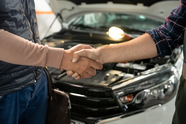 Professional handshake between car buyer and seller in automotive workshop, illustrating successful used car resale business transaction for car flipping beginners