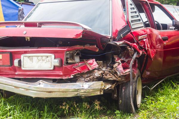 Severely damaged red car with a crushed rear quarter panel showing the salvage car risks and structural damage typical of a salvage title car after a serious accident