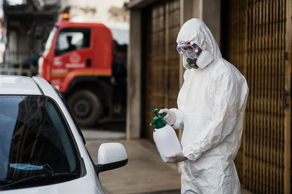 Worker in protective suit spraying disinfectant on junk cars with biohazard and performing professional biohazard cleanup for secure purchase of contaminated auction cars