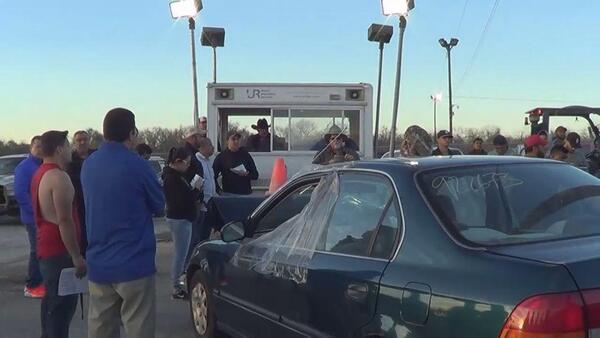 Bidders gathered around a used car at a cheap car auction in Dallas TX
