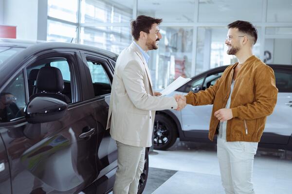 Car salesman and buyer shaking hands at a dealership illustrating the best time to buy a car and how to get the best deal on a car