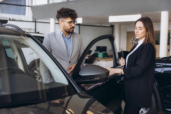 emale salesperson showing a car to a male customer at a dealership illustrating key car buying tips and choosing the best day to buy a car