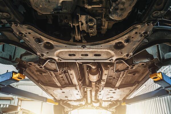 Close-up undercarriage view of a car raised on a workshop lift showing the frame and mechanical components inspected to qualify for high risk auto insurance and comprehensive coverage rebuilt title policies
